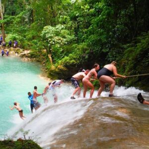 VibraGem Tours Blue Hole Tour in Jamaica with a group of tourist holding a rope walking down the falls.